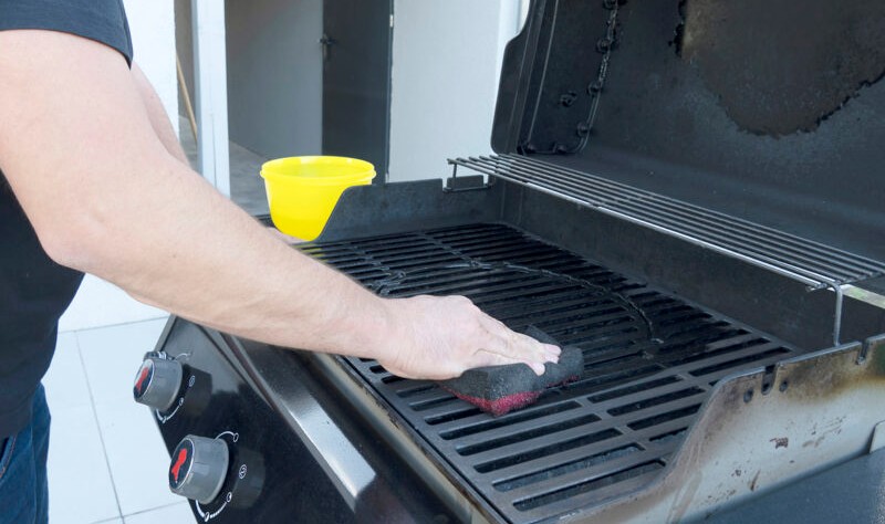 young man wiping grill grates with a sponge
