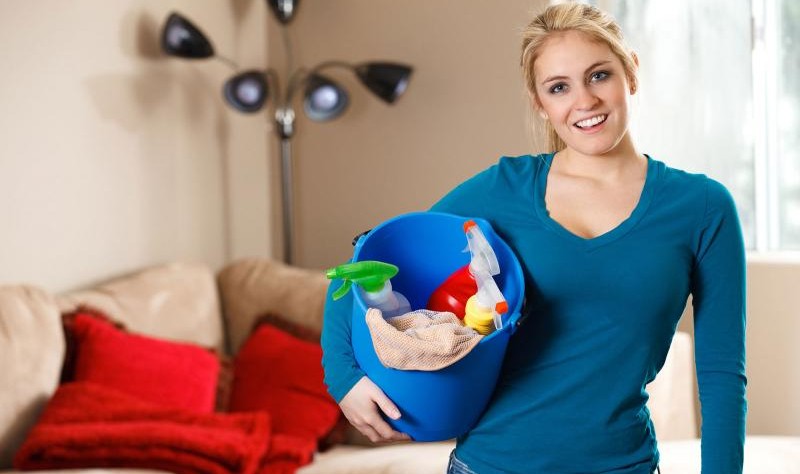Young woman holding a bucket full of spray bottles and chemicals