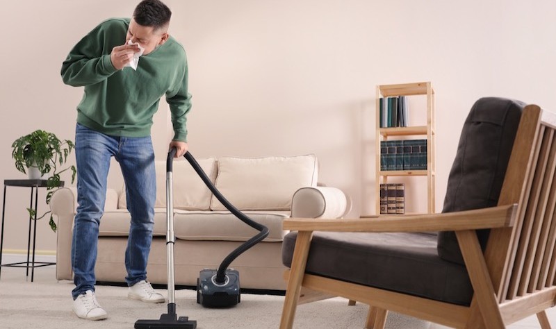 young man suffering from allergies and vacuuming the house