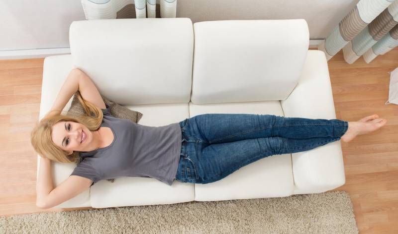 Woman in t-shirt and blue jeans relaxing on her sofa inside a hall