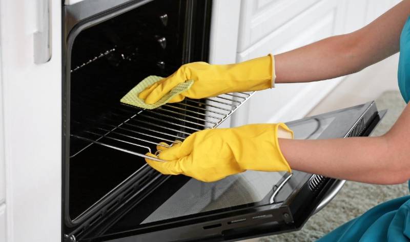 Woman hand in yellow gloves scrubbing oven rack with cloth