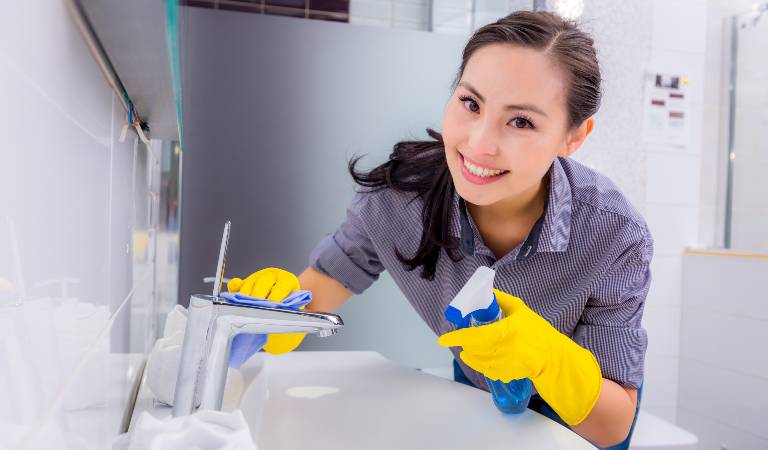 Woman in shirt and yellow gloves cleaning inside a bathroom