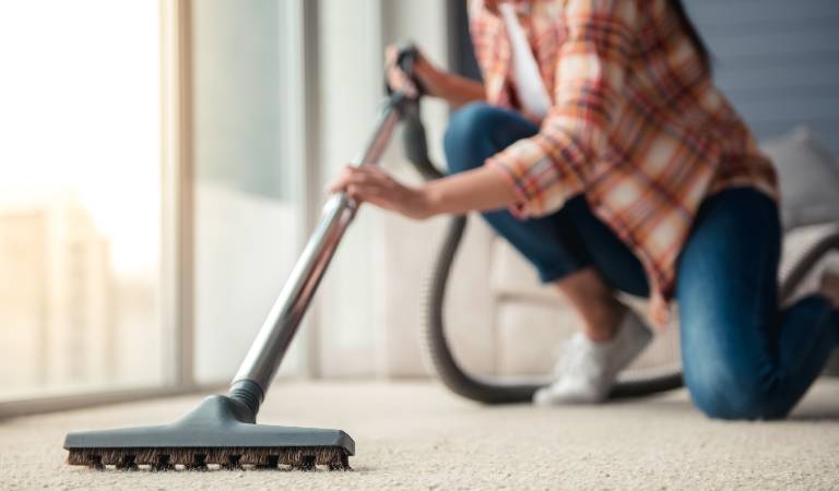 Woman in check shirt and blue jeans vacuuming floor
