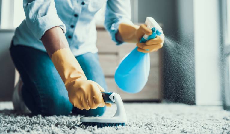 Woman in shirt and jeans holding a blue bottle spraying on her carpet