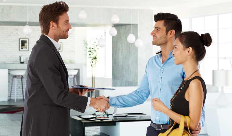 Young couple and home owner shaking hands, smiling.