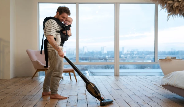 Full shot father holding baby while vacuuming