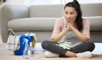 Young woman looking bored sitting on the floor while doing cleaning chores at home
