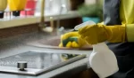 person in yellow rubber gloves cleaning house washes induction stove with sponge