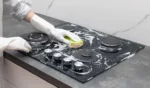 Female hands in rubber gloves cleaning gas stove with detergent household cleaning concept