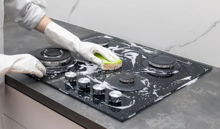 Female hands in rubber gloves cleaning gas stove with detergent household cleaning concept