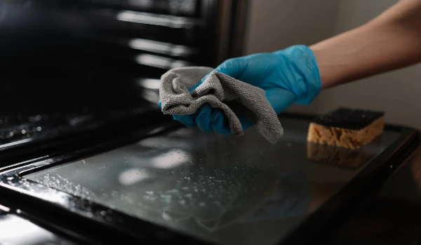 Closeup hands in gloves wiping oven glass door using microfiber