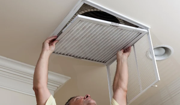 Senior male reaching up to open filter holder for air conditioning filter in ceiling for cleaning