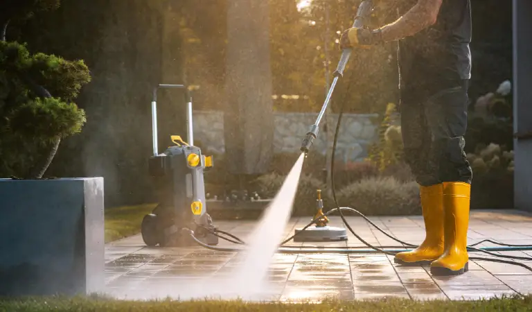A person power washing a patio with a pressure washer in a sunny outdoor setting