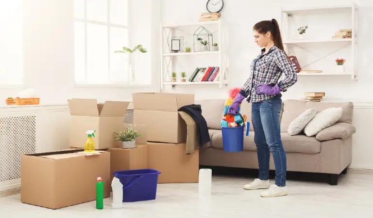 Young woman tiding up after moving to new appartment. Girl with various detergents, rags and mops in living room full of carton boxes