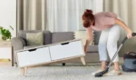 Woman vacuum and dust or dirt removal at home female cleaner lifting table and vacuuming for clean rug mat or floor in the lounge